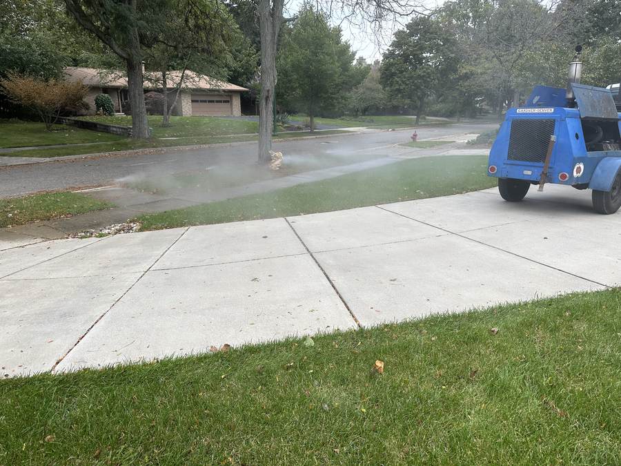 Air compressor trailer running a sprinkler blowout on a residential lawn